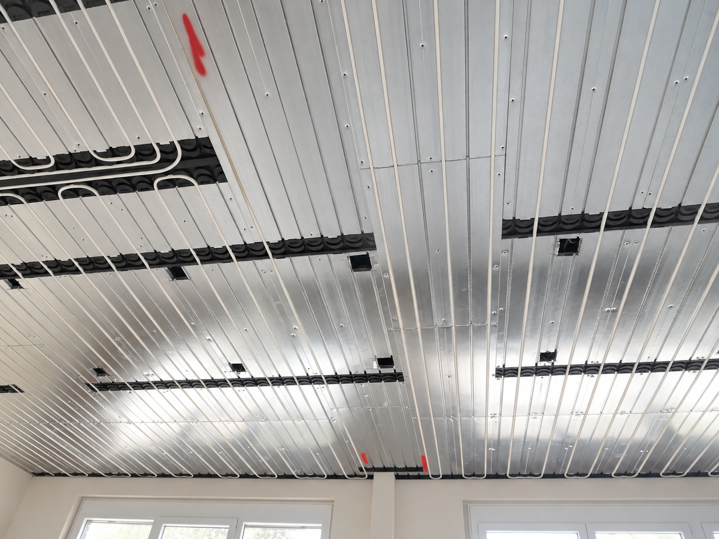 Wassergeführte Deckenheizung mit Aluminiumprofilen und sichtbaren Heizrohren vor der Verkleidung